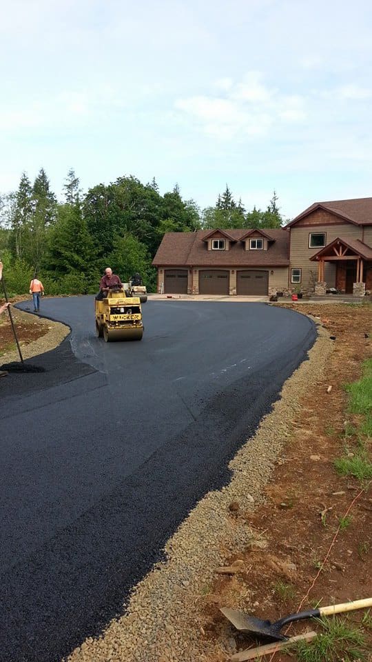 Man on road roller paving road in front of brown house